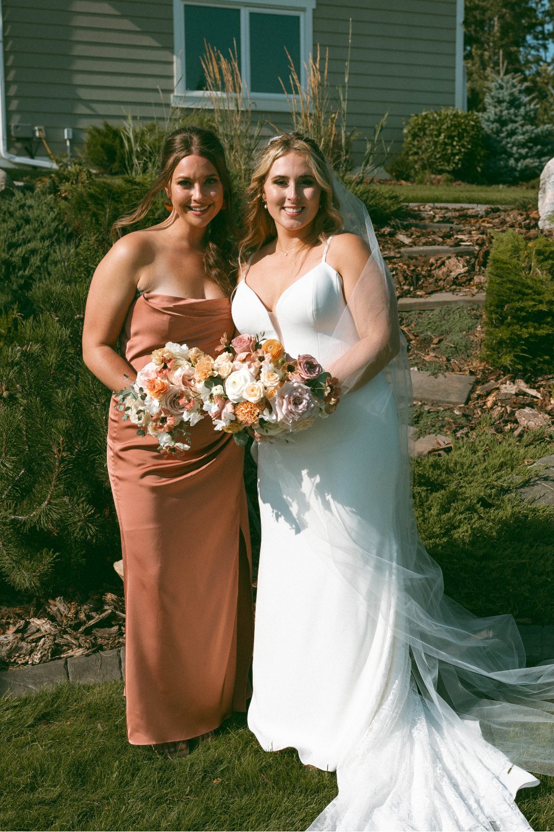 Katrina and a bridesmaid smiling in the summer sun, holding their bouquets.