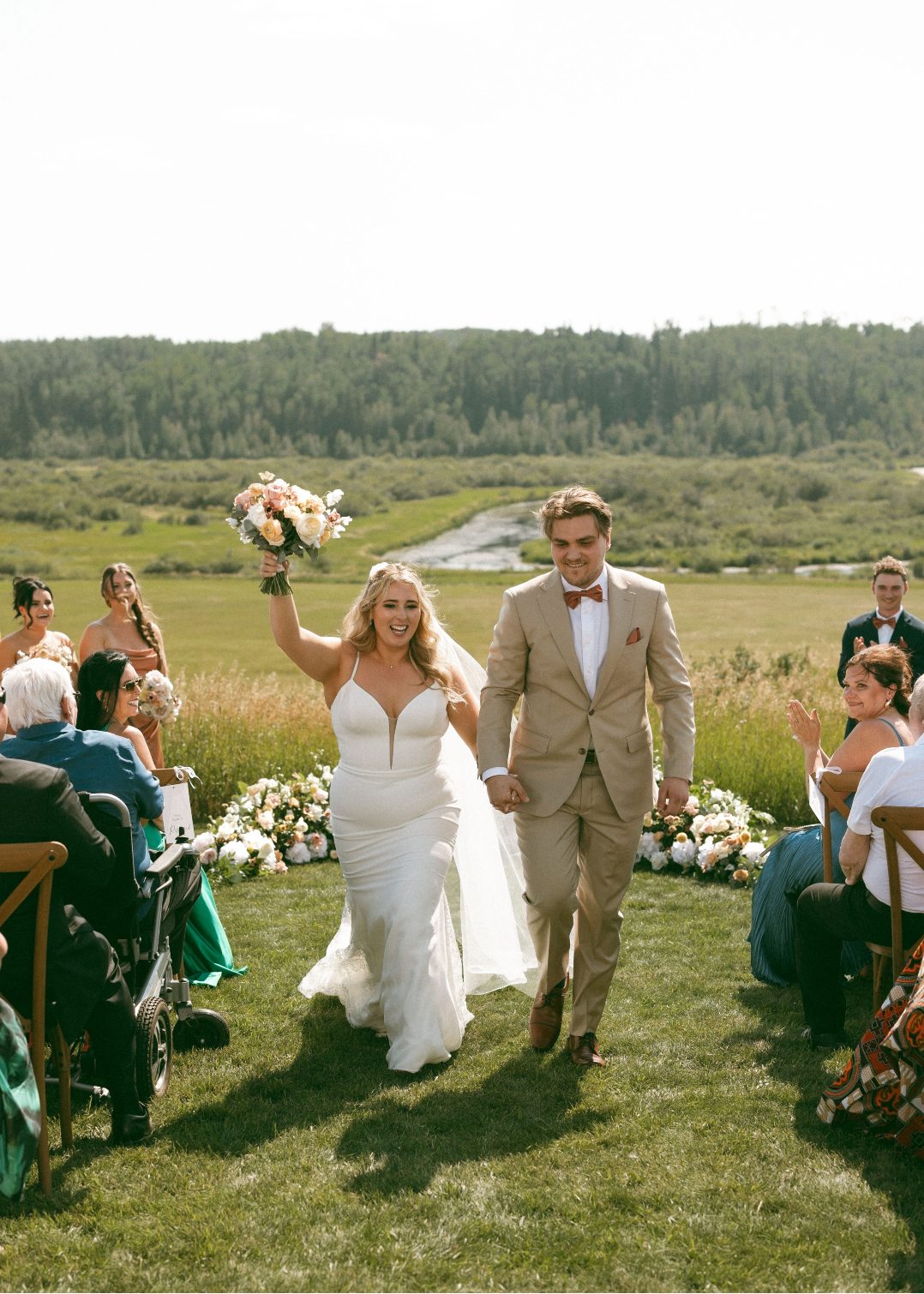 Katrina holds her bouquet high in the air cheering as her and Connor come down the aisle.