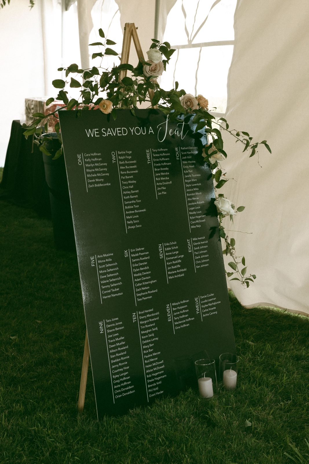 The seating chart for the reception is accented with some greenery elegantly draped across the top and accented with a couple blooms.