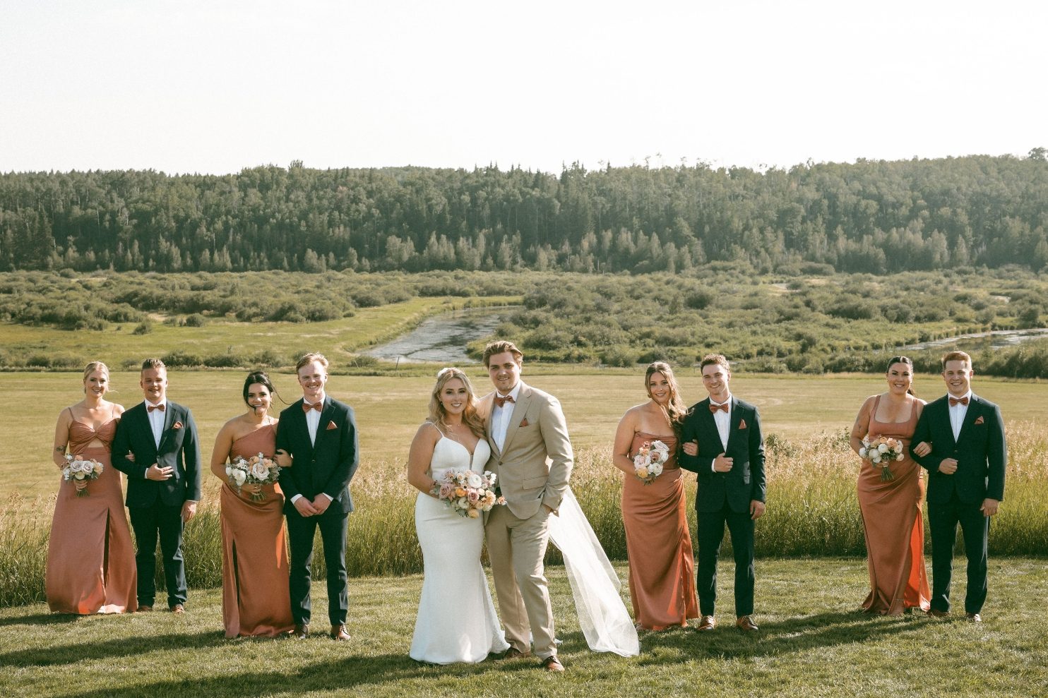 Katrina and Connor with their wedding party standing in pairs with the scenic background behind them.