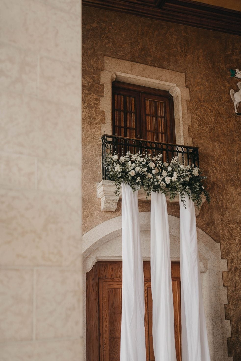 A stone balcony draped with long white fabric and overflowing with white roses and greenery.