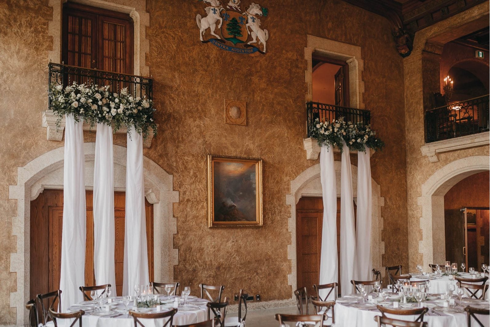 The reception hall at Banff Springs styled with draped white fabric, lush greenery and round tables with white linens.