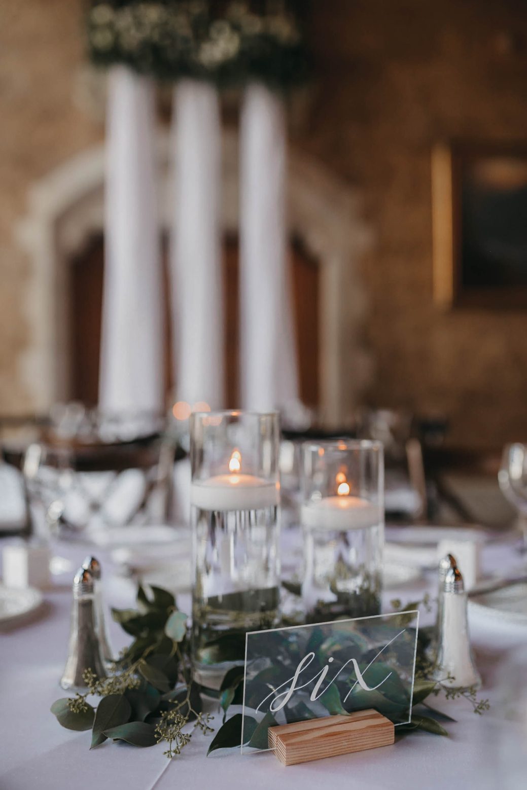 Elegant wedding table set with floating candles, eucalyptus and a modern acrylic table number reading "six."