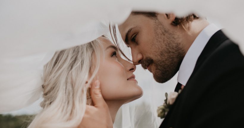 A romantic close up of the couple under a sheer veil, foreheads gently touching as they gaze into each other's eyes.