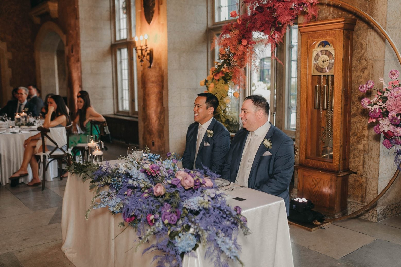 The newlyweds sit smiling at their sweetheart table beneath the rainbow arch during the reception.