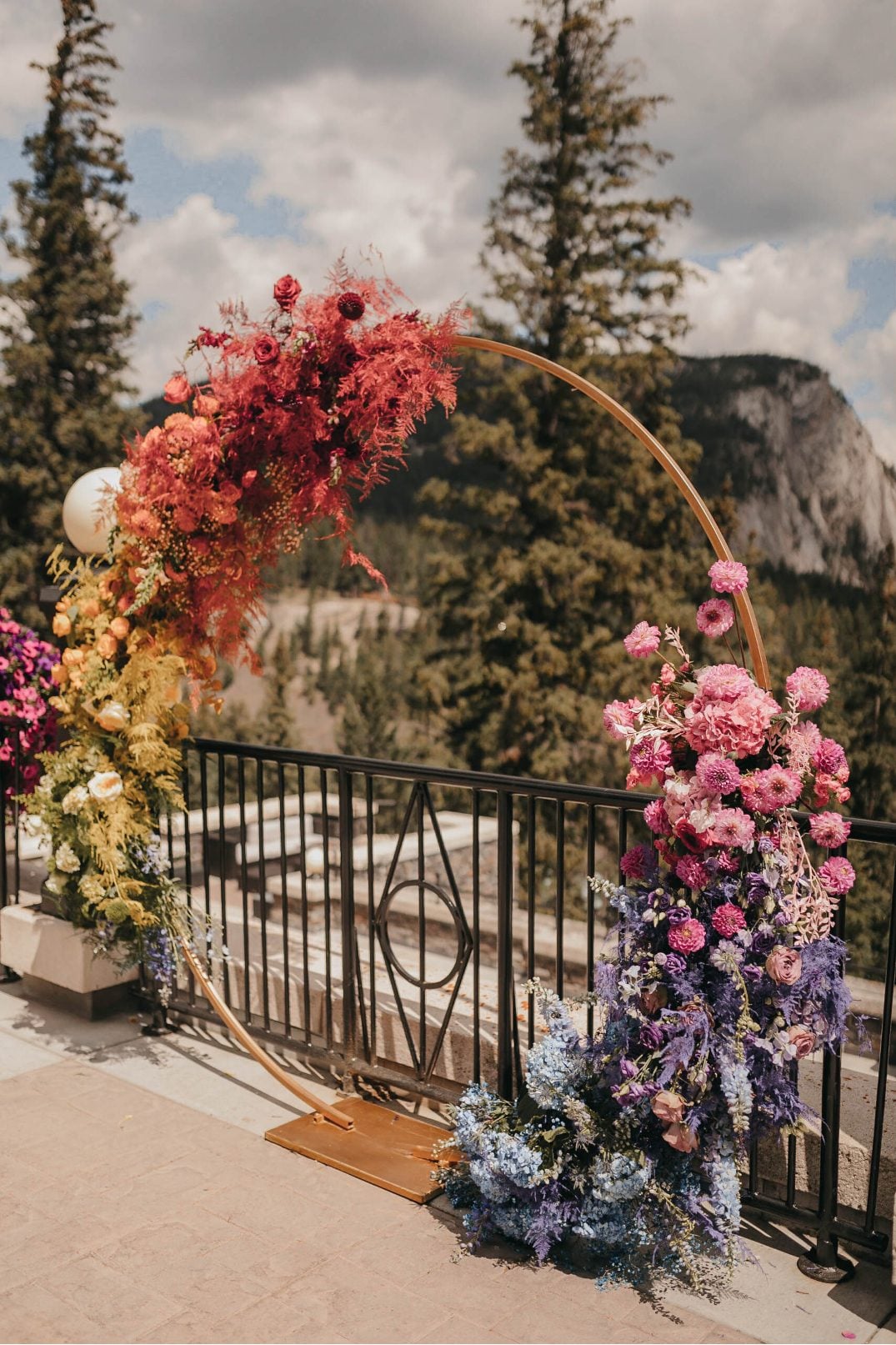 Detail view of the rainbow floral arch showing vibrant blooms in red, orange, yellow, pink and purple.