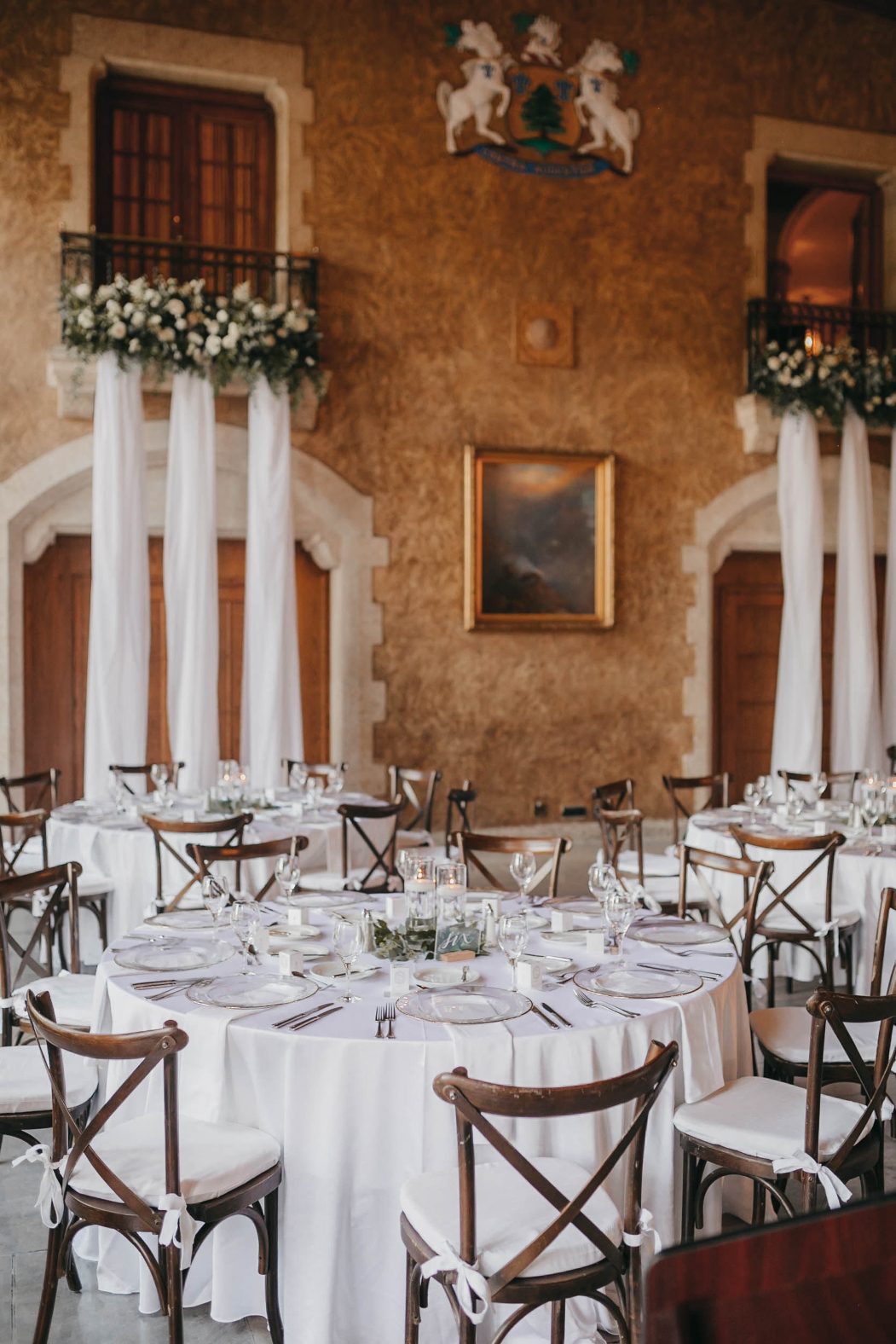 A wide view of round reception tables beneath floral draped balconies and a historic crest at Banff Springs.