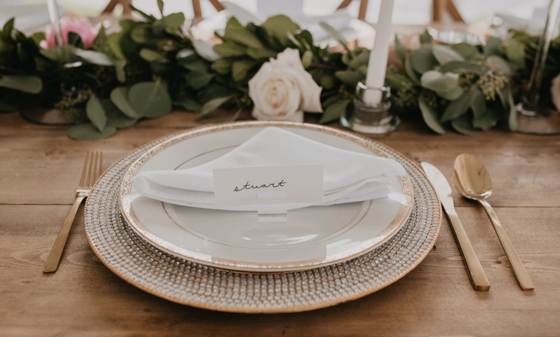 A beautifully syled wedding place setting with gold accents and a handwritten place card reading "Stuart"