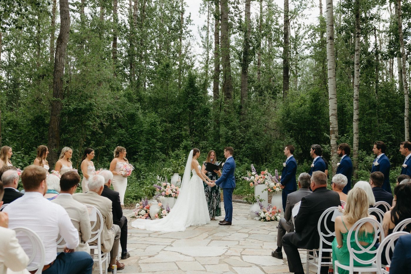The bride and groomhold hands during their ceremony at Sparrow Lane, standing between pastel floral arrangements.