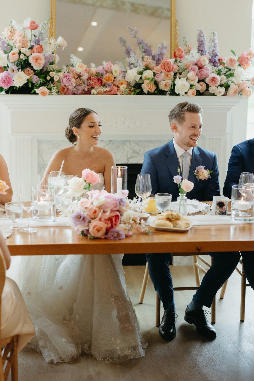 The bride and groom sitting at the head table smiling happily with beautiful flowers displayed in front and behind them.