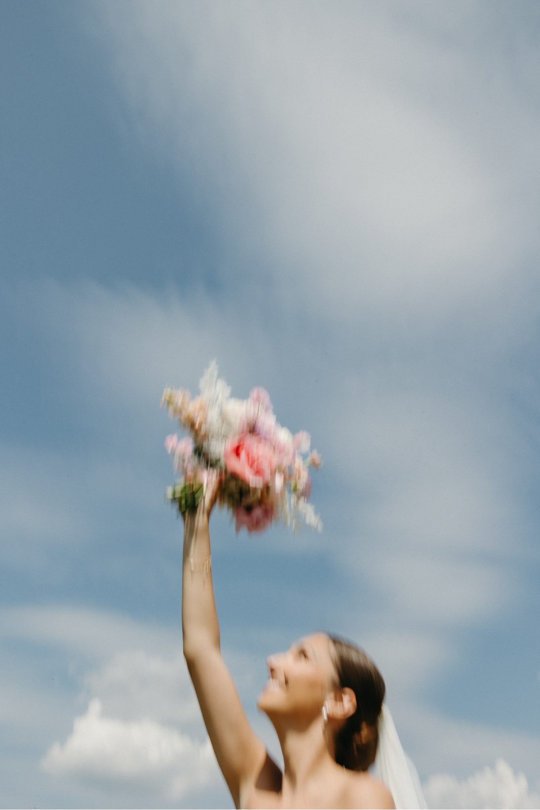 An artistic motion blurred photo of the bride holding her bouquet high against a dramatic sky, symbolizing celebration and freexom.