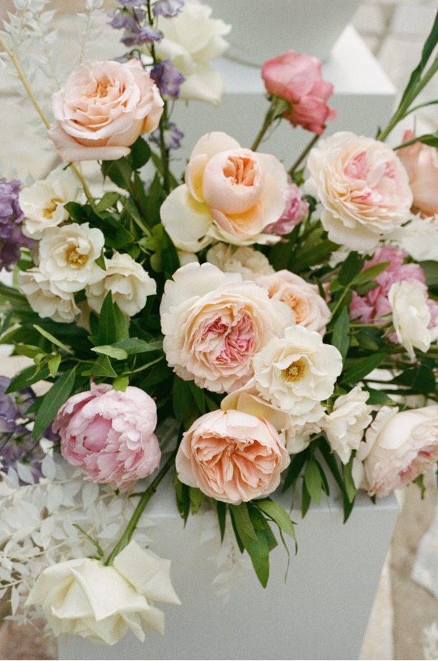 A close up of one of the floral arrangments of garden roses, peonies, spray roses, delphinium and bleached ruscus.