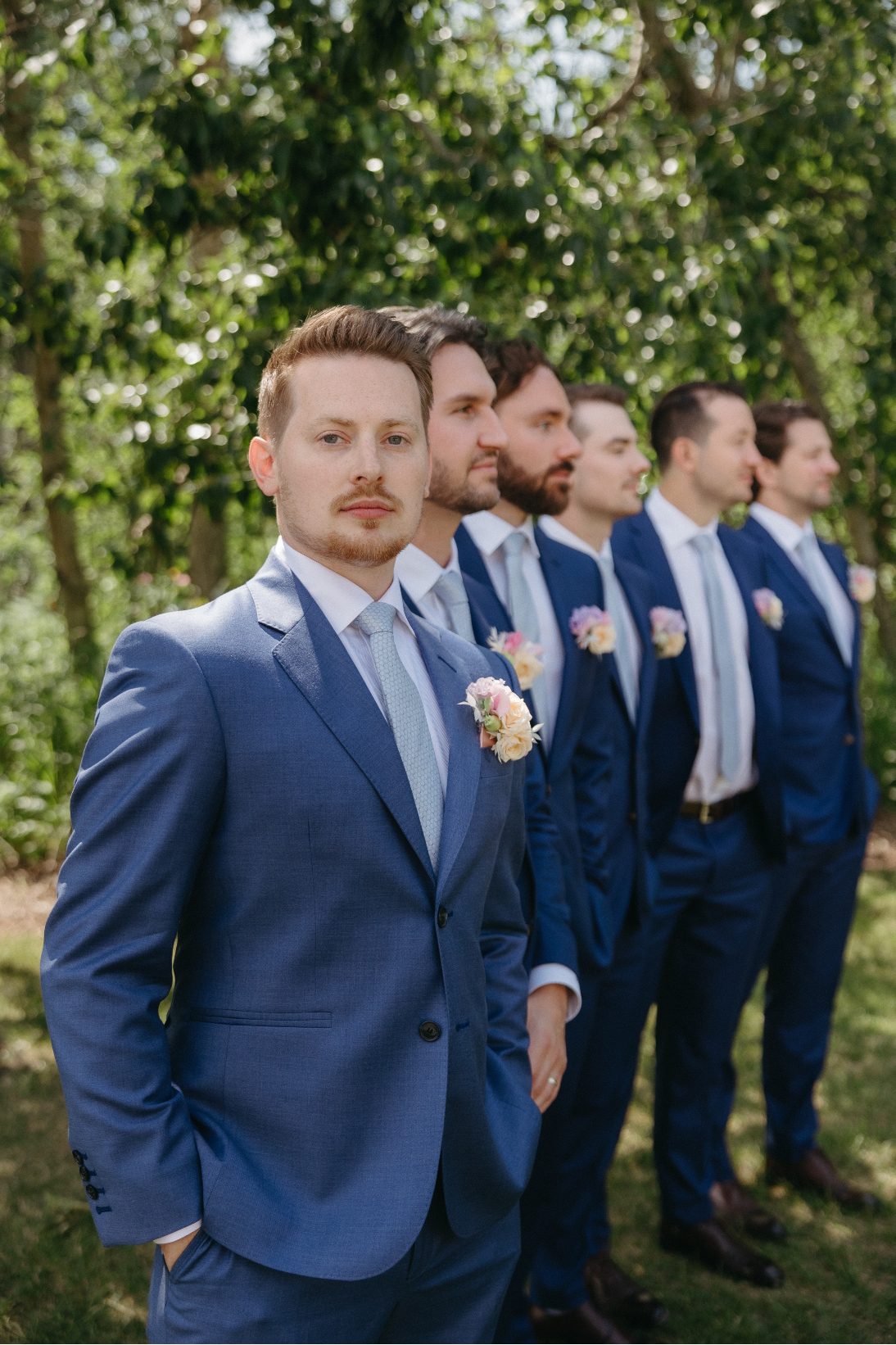 The groom looks at the camera and stands next to all the groomsmen while they wait for the bride to enter.
