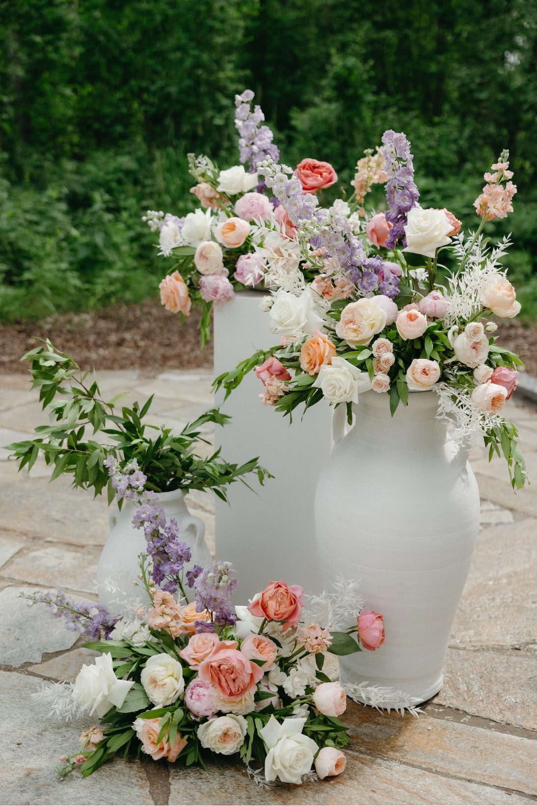 An artfully arranged cluster of arrangements on top of a pillar and urns in romantic pastel tones.