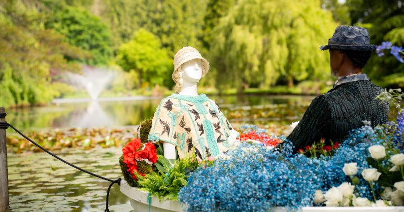 Close up of the LAdy Rose mannequinn wearing a floral textured cream and turquoise dress in a flower filled boat on the pond with a fountain in the background.