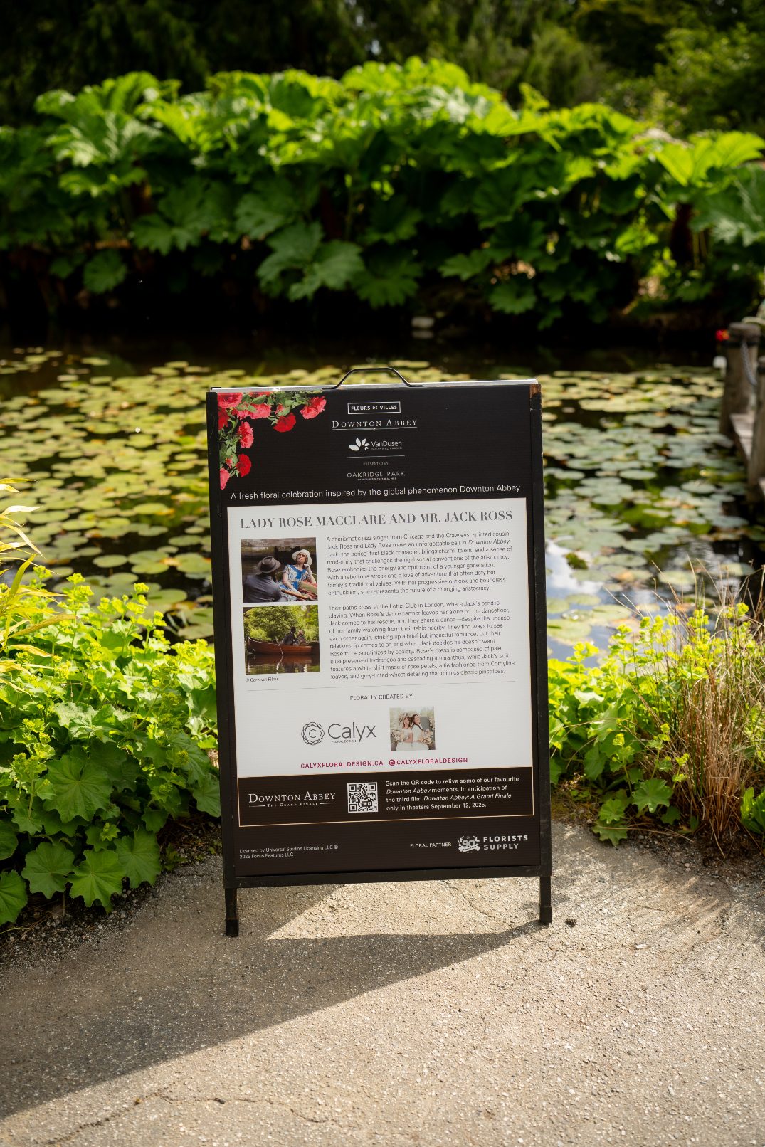 A black event sign with Downton Abbey and Fleur De Villes branding beside the floral installation introducing Calyx Floral Design and detailing the inspiration.