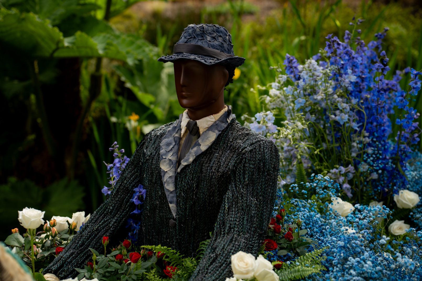 Close up of Jack Ross mannequin seated in a boat surrounded by lush floral arrangements and greenery at Fleur De Villes event at VanDusen Botanical Gardens.