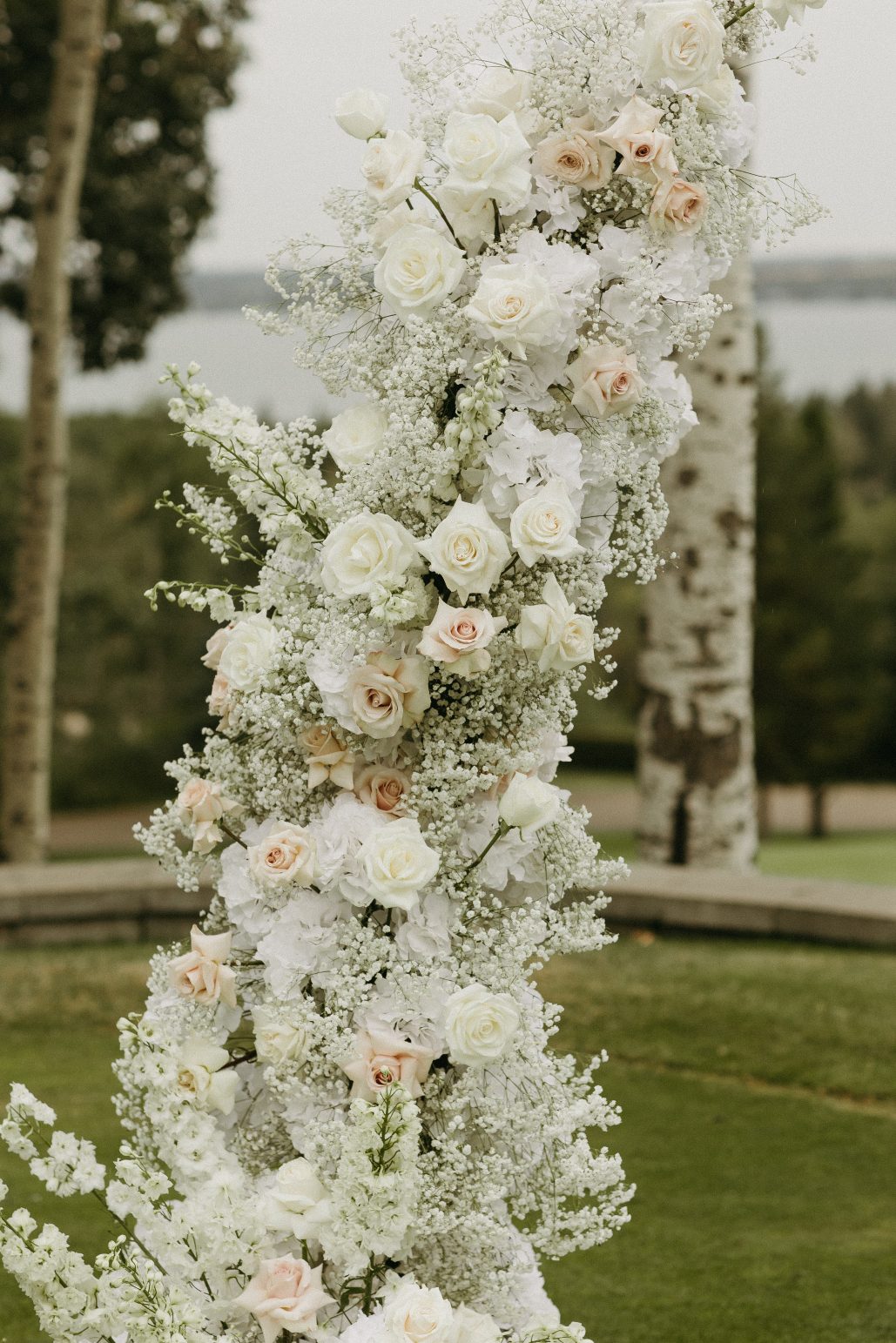 Close up of a floral arch with an abundance of cream, blush and white roses, baby's breath and hydrangea arranged on a curved structure.