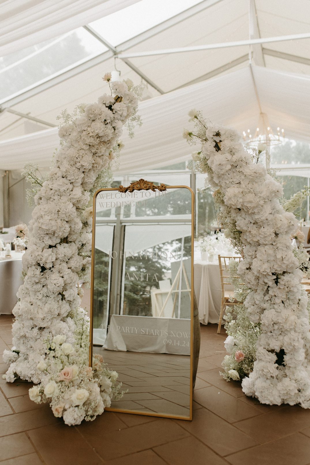 Gold framed mirror surrounded by lush white floral pillars at the indoor reception at Hilltop Wedding Center.