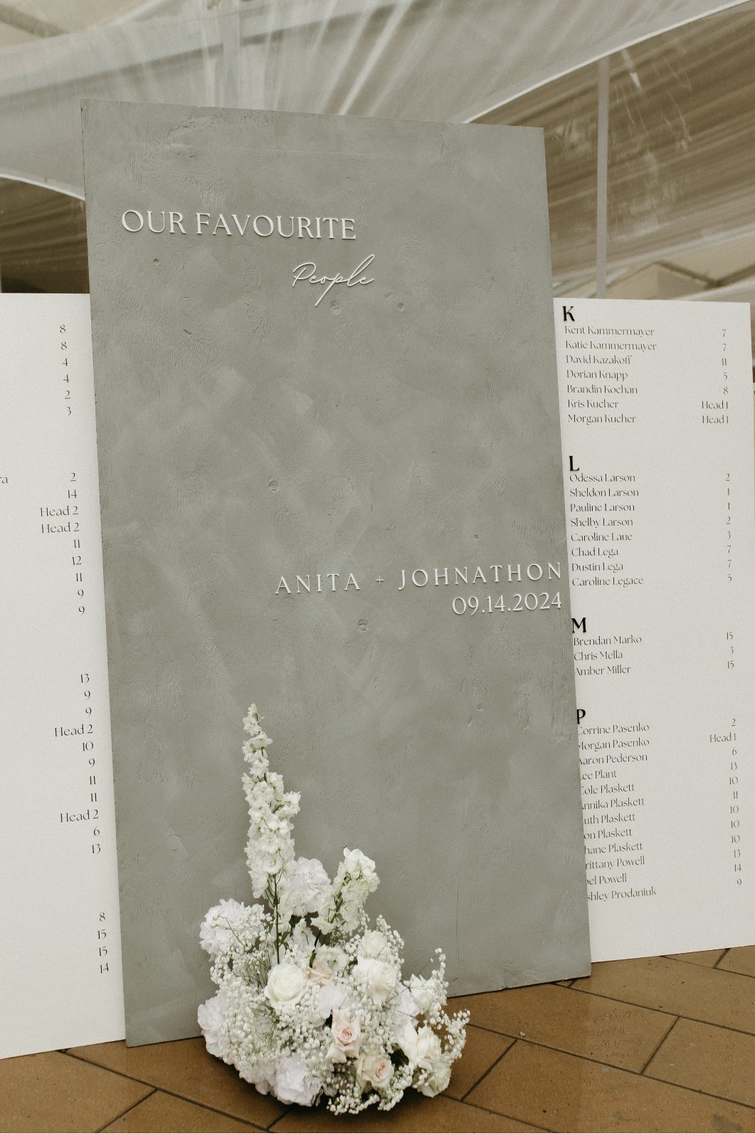 Concrete wedding seating chart display reading "Our Favourite People" with guest names and a blush and white floral arrangement at the base.