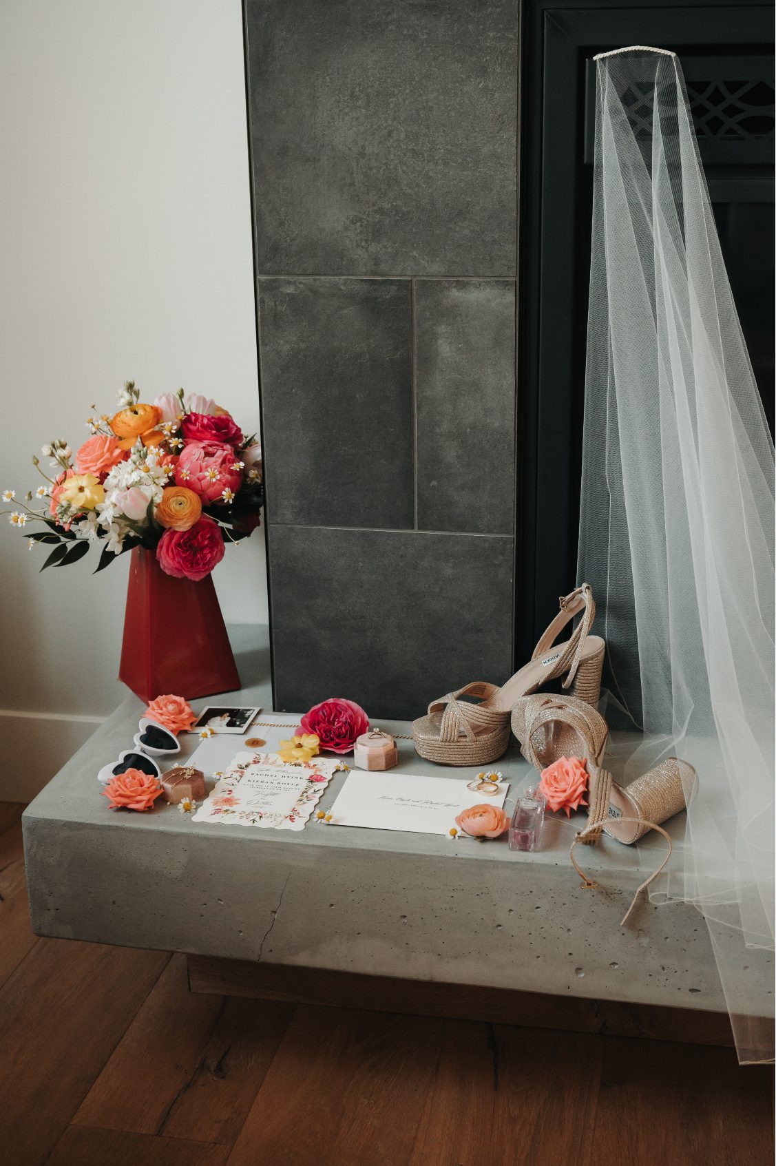 Flat lay of bridal details including wedding shoes, veil, jewellery, coral blooms and invitations styled beside the bouquet.