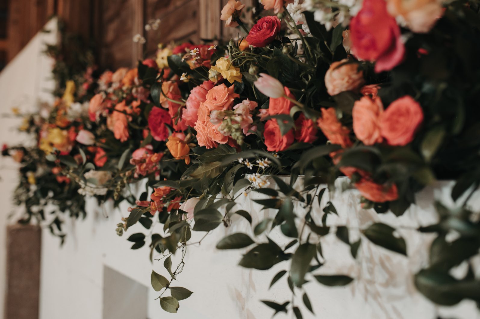 Close up of vibrant altar floral arranagement featuring coral roses, bright ranunculus, chamomile and trailing greenery.