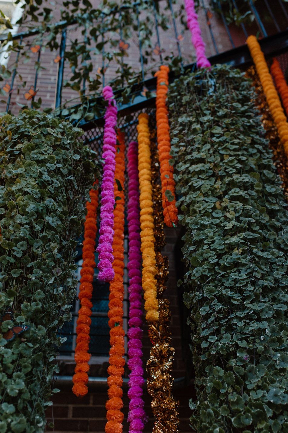 Bright marigold and magenta floral garlands cascade besides lush greenery for a bold vertical installation.
