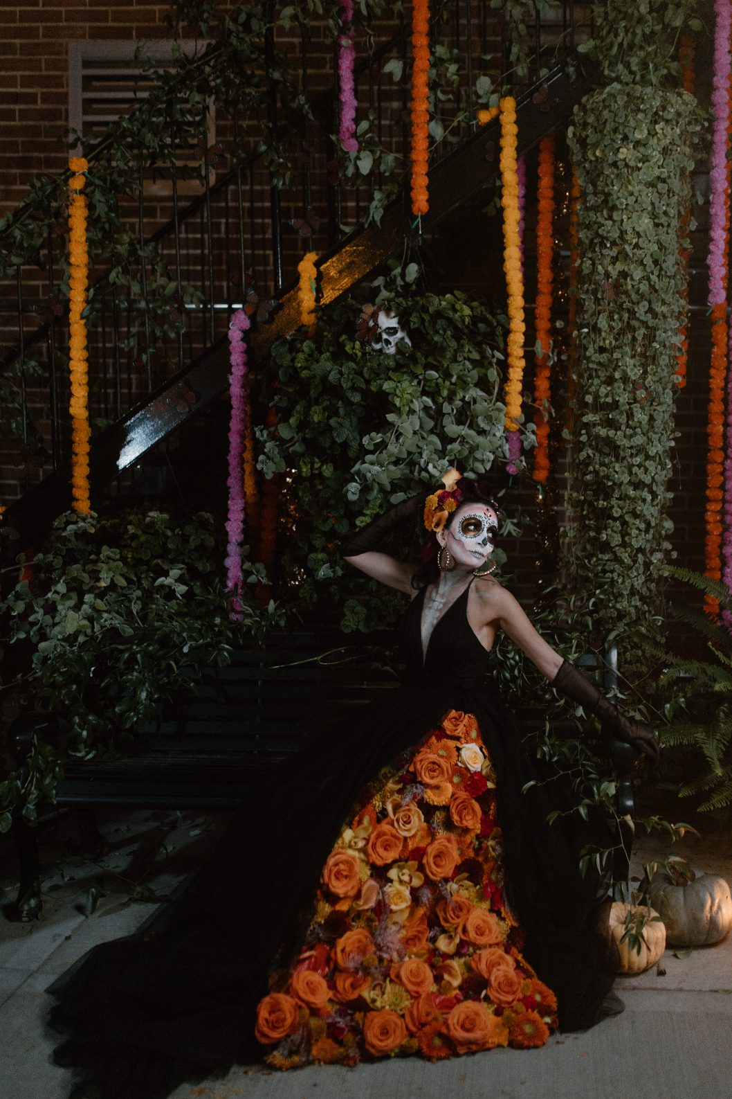 Model in dramatic black gown adorned with stunning orange floral panel in her dress poses beneath cascading marigold and greenery garlands.