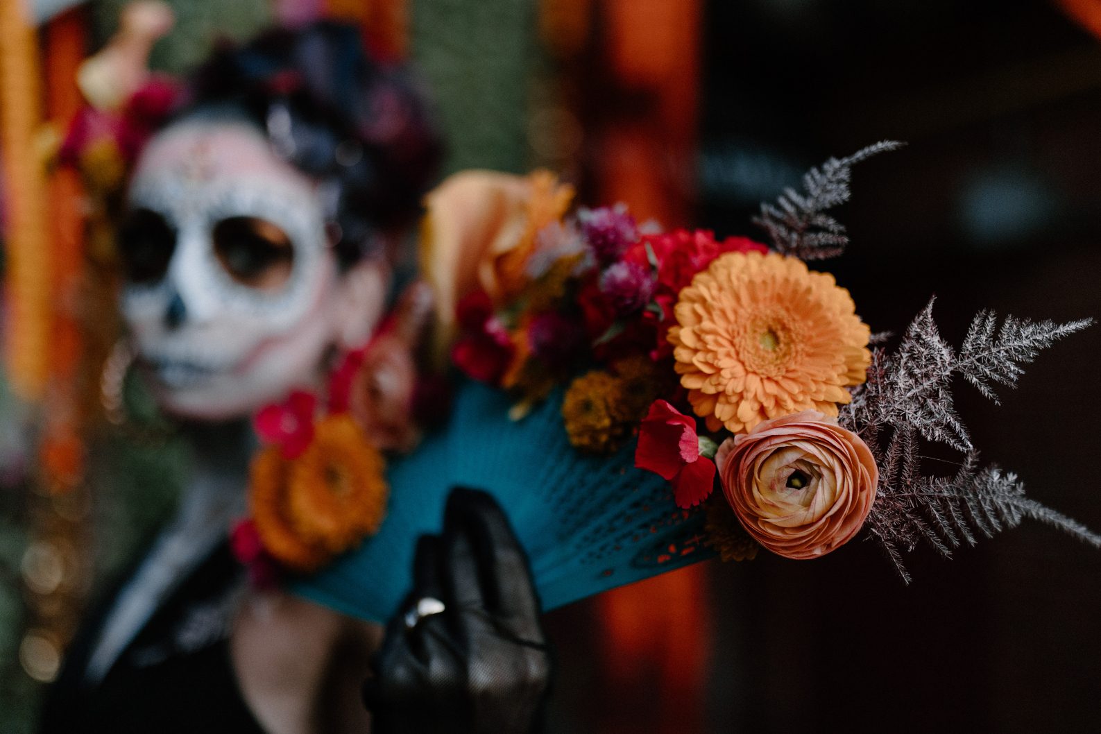 Close up of model's floral fan in bold orange and coral hues, offset with teal lace details on the fan and soft silver fern accents.