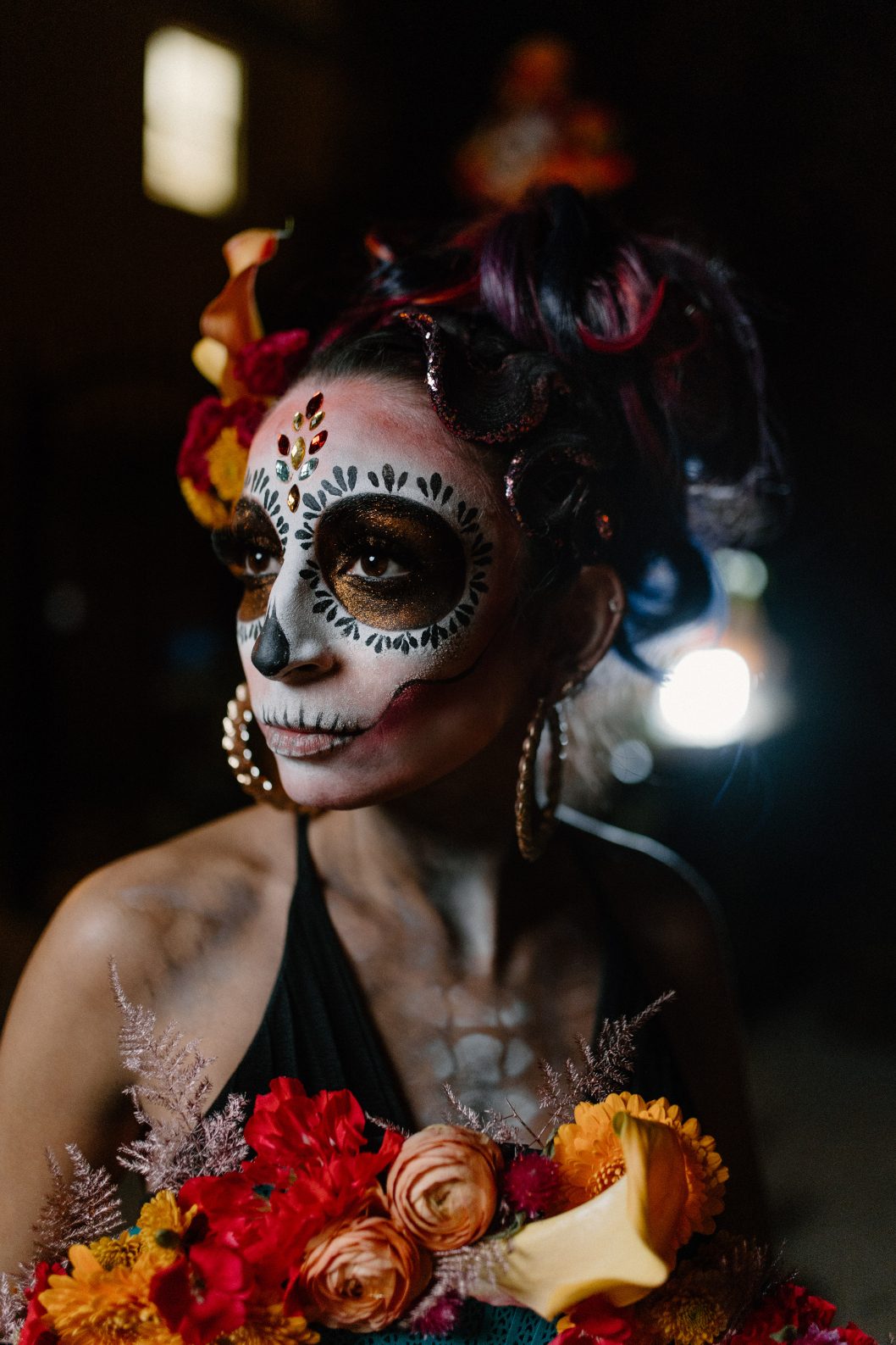 Model with elaborate sugar skull make up holds vibrant bouquet and gazes softly into the nights light.