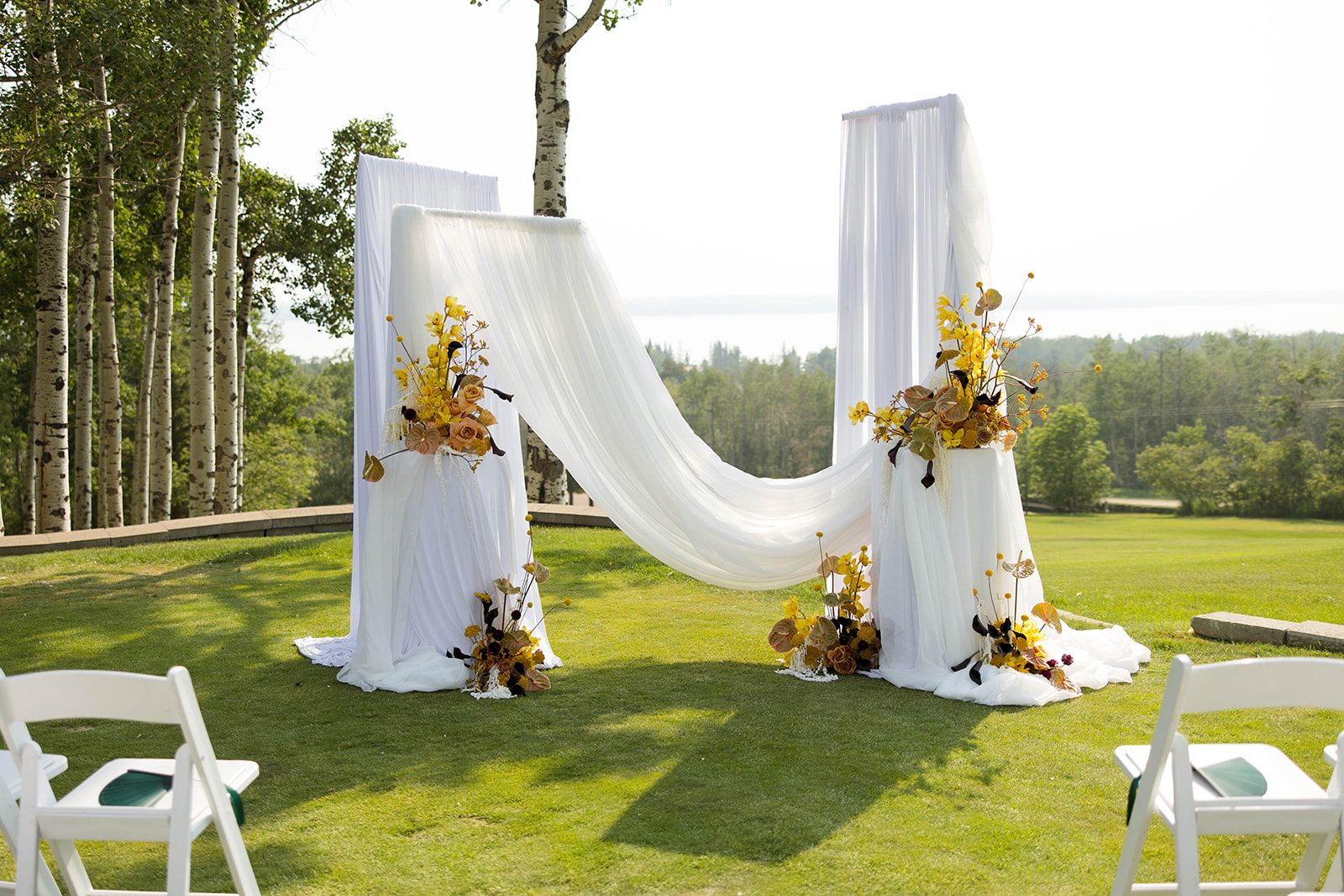 The ceremony set up was stunning, some panels of white fabric draping beautifully in the sunny lakeview outdoor location. Several artistic arrangements in bold yellow, dark purples and neutral tones accented the space perfectly.