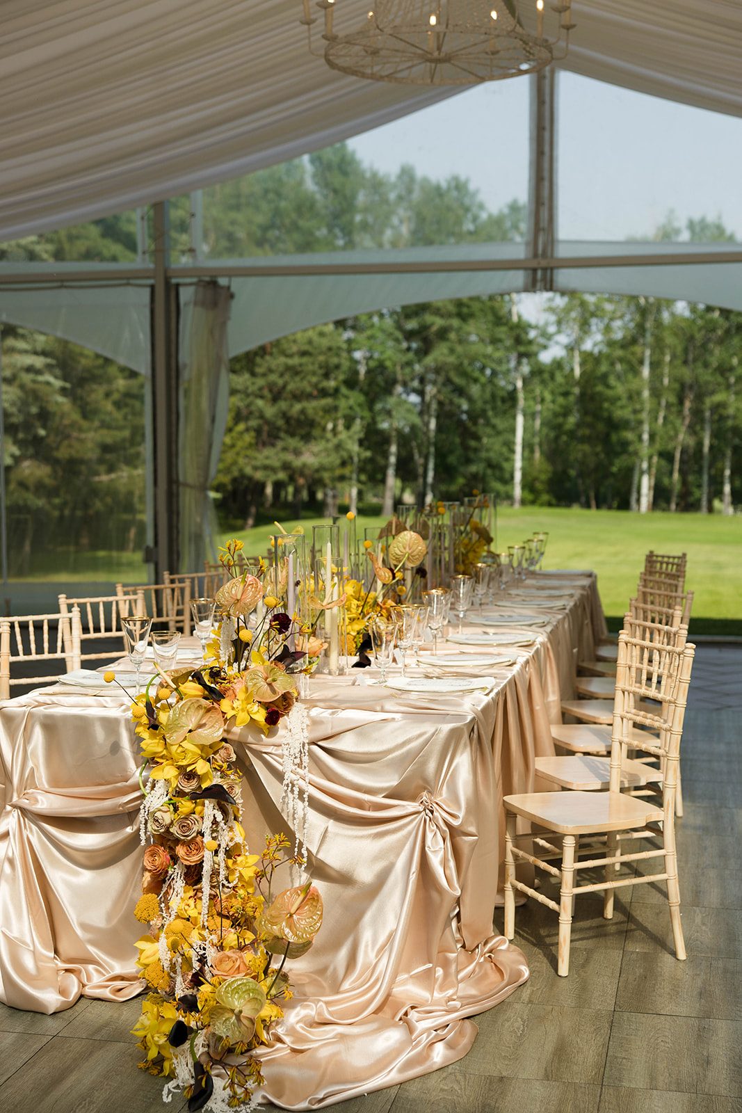 The full tablescape showing the chairs neatly lined up, multiple arrangements down the length of the table and cascading over the front with soft draping champagne satin.