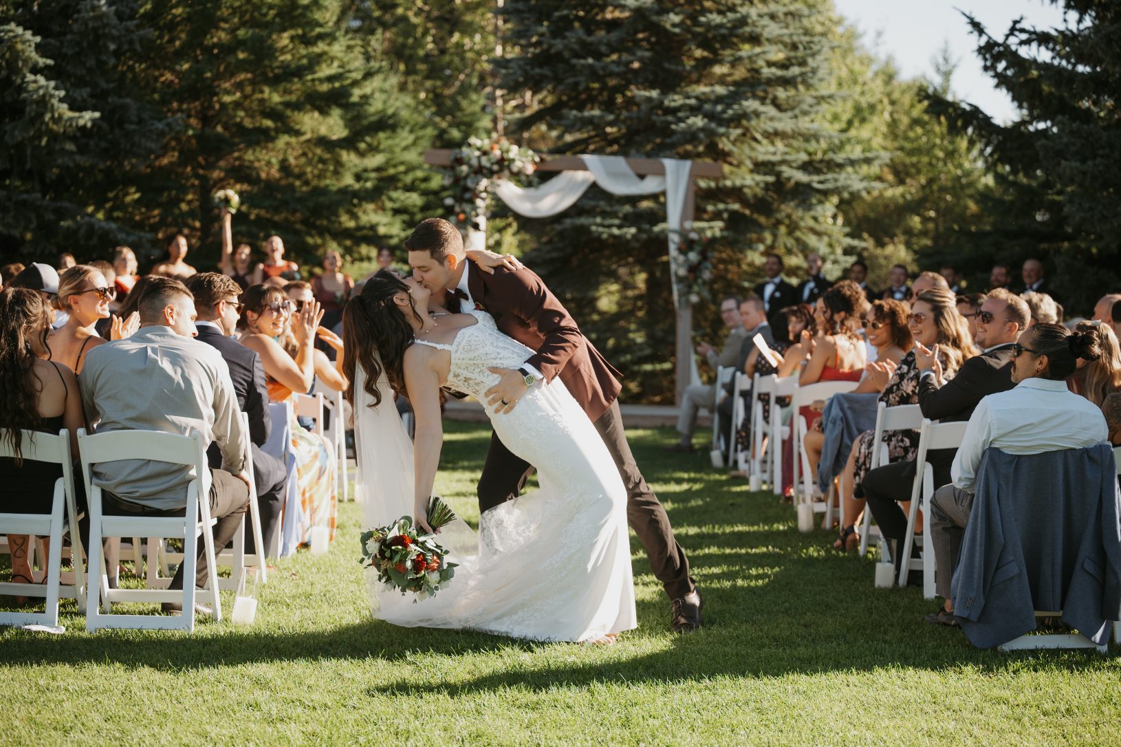 Groom dips the bride into a romantic kiss during their recessional as guests cheer from both sides of the aisle.