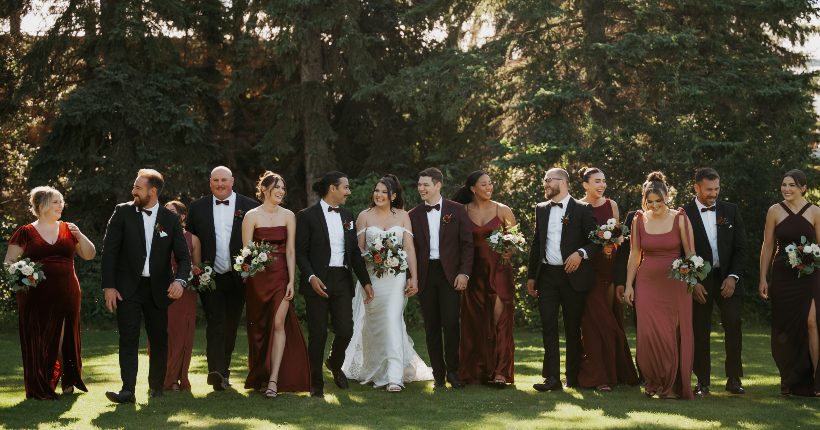 Bride and groom standing in a line with their bridal party, dressed in formal attire laughing and smiling with each other.