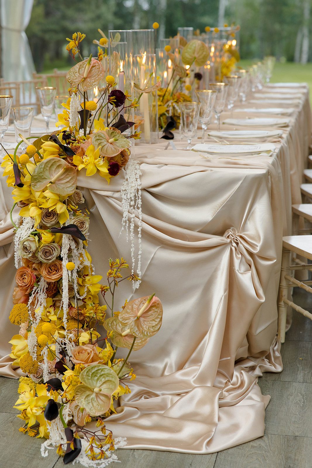 Dramatic floral cascade of yellow orchids, caramel coloured roses, anthurium and hanging amaranthus flowing over draping champagne satin linens.