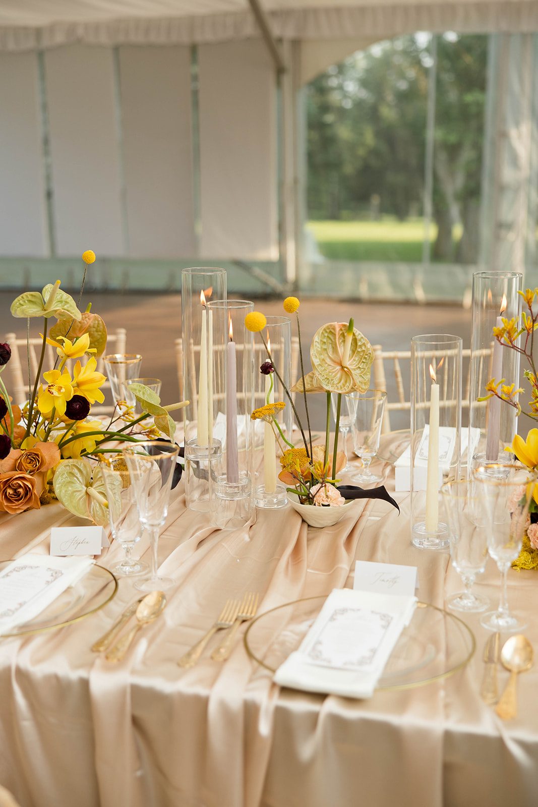 Tall taper candles and sculptural ikebana inspired arrangements of yellow styled on draping champagne satin table linens.