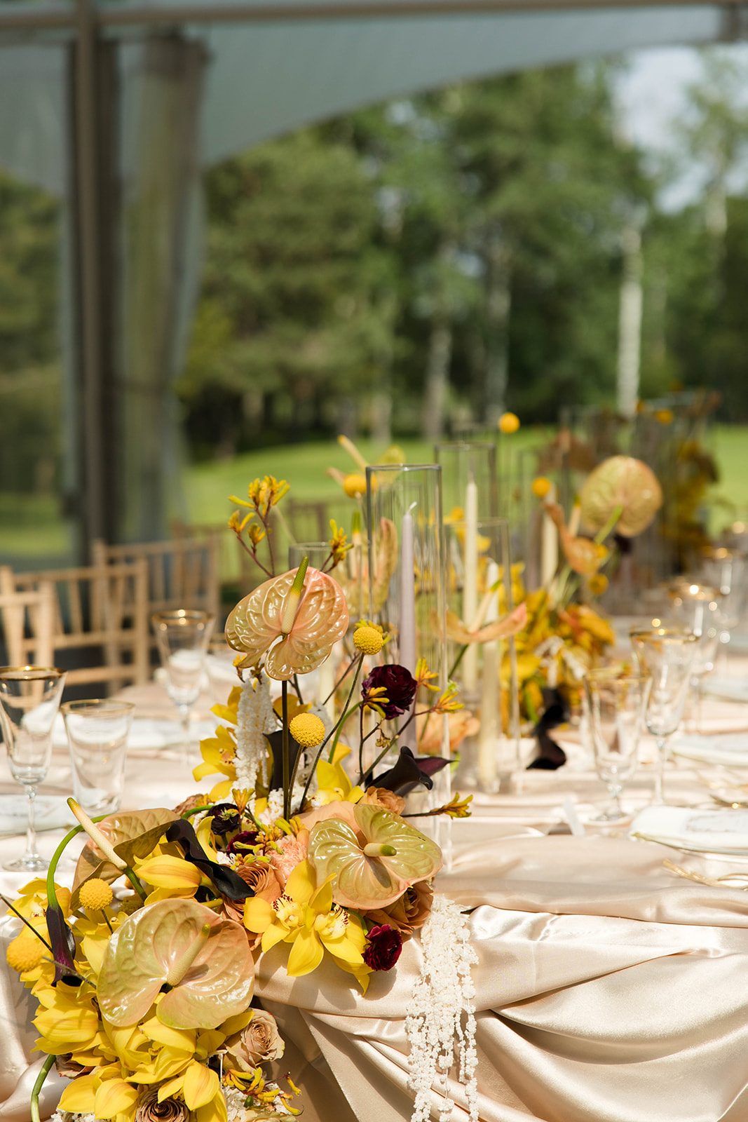 A detail shot of the sunning flowers cascading over the edge of the tablescape including anthurium, craspedia, kangaro paw, cymbidium orchids, roses, ranunculus, calla lilies, dried yarrow and hanging amaranthus.