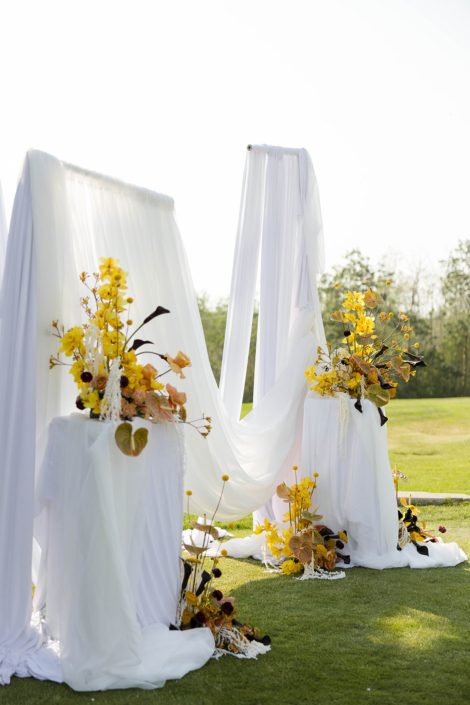 From the same photoshoot as the last photo, the Ceremony set up at one of Hilltop's outdoor locations, with tons of white draping fabric for a dramatic and romantic feel with several arrangements at different levels on either side in bold colours.