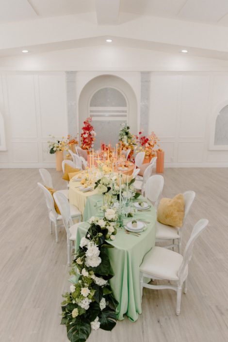 The table set up from above, showing beautiful centrepieces designed down the table, broken arch in bold oranges and corals behind and a waterfall of greens flowing down the front of the table.