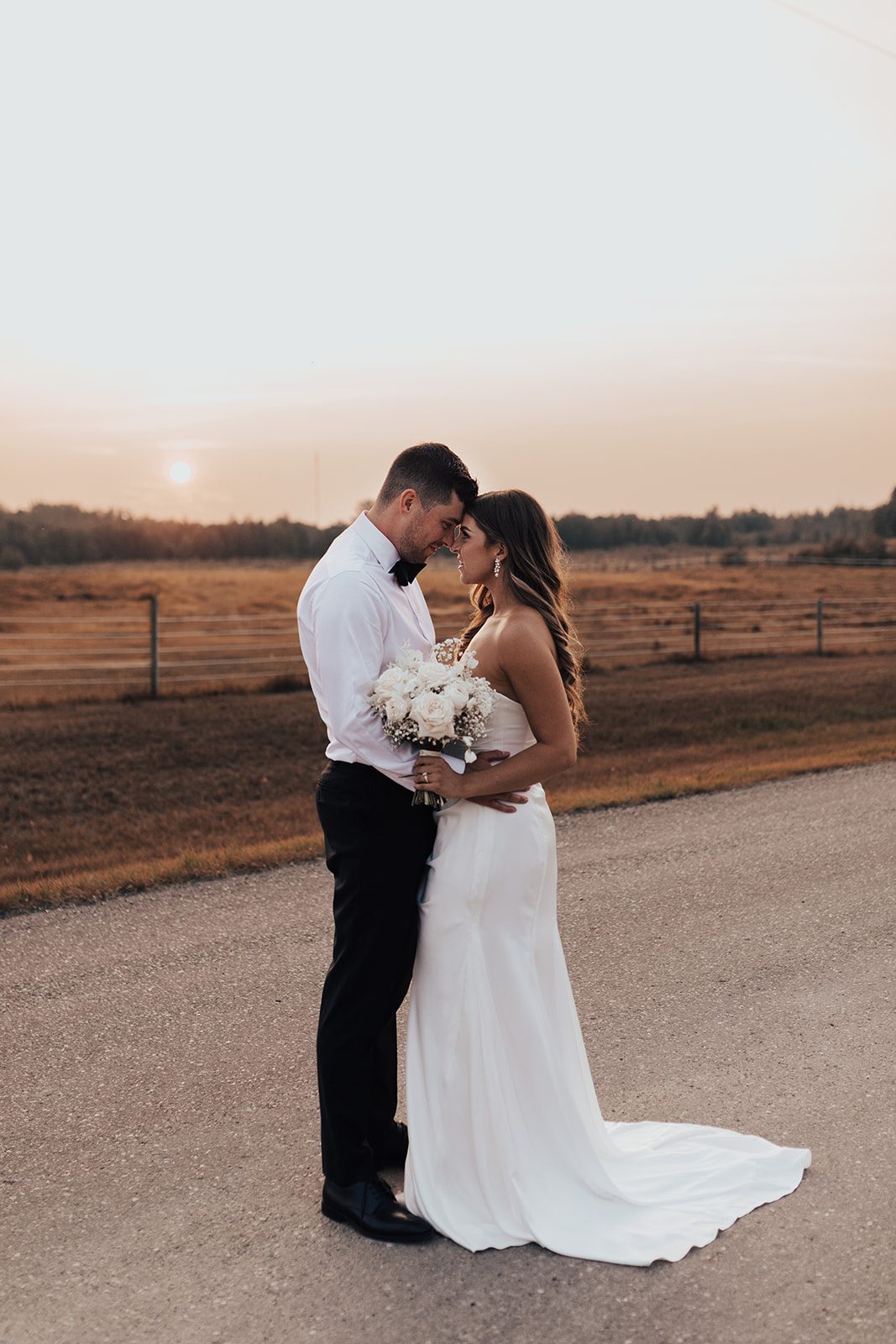 Mr + Mrs Day Bride and groom standing with their foreheads together at sunset with the sky softly glowing behind them.
