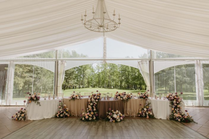 Inside the tent at Hilltop Wedding Centre a serpentine table set up with ombre linens getting darker towards the centre. Floral arrangements on top of the tables, one water falling down over the table and several on the floor to highlight the stunning head table.