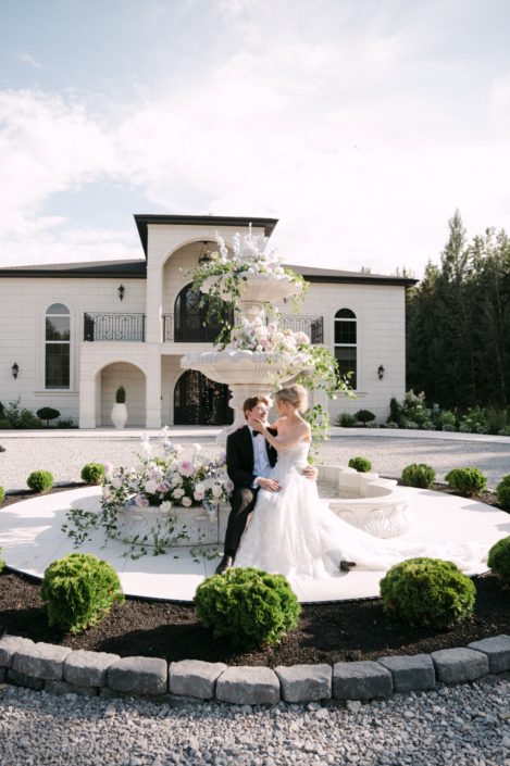 A beautiful calyx couple sit at the edge of the fountain in front of Archway Manor, gazing lovingly at each other and surrounded by beautiful cascading arrangements sitting in the different layers of the fountain.
