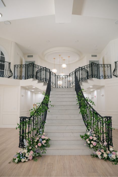 The dramatic staircase inside Archway Manor with huge arrangements at the base with lush green wines weaving up the banisters for an organic feel.