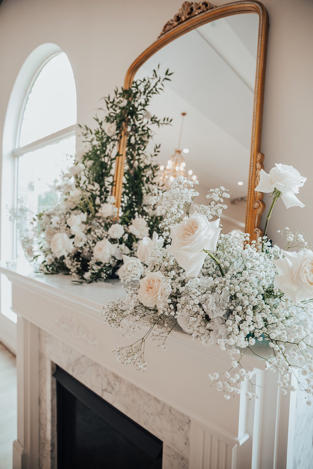 Mr + Mrs Day Close up of the arrangements on the mantle of the fireplace displayed on either side of the gold mirror, featuring baby'ss breath, roses, ranunculus and lush greenery.