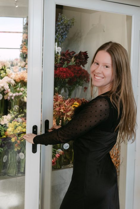 New Calyx staff member, Olivia, turned and smiling at the camera as she opens the doors to the flower bar.