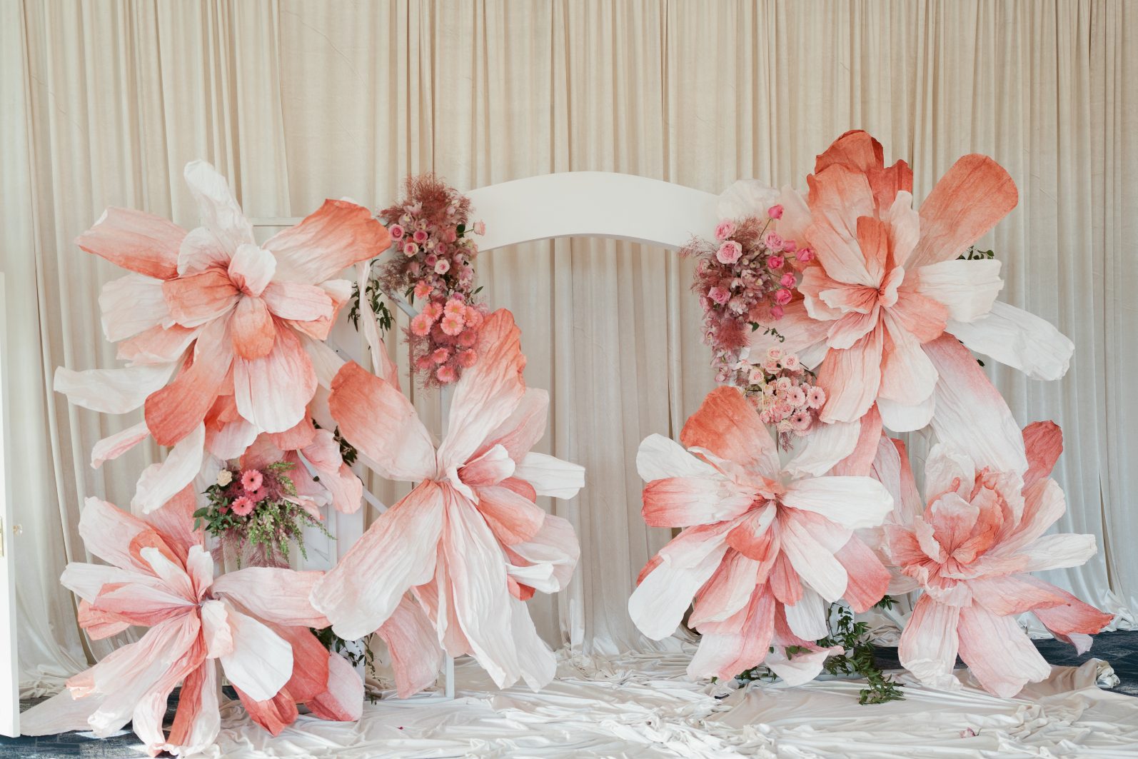 A huge arch featuring massively oversized pink paper flowers, with clustered groupings of fresh flowers strategically tucked throughout.