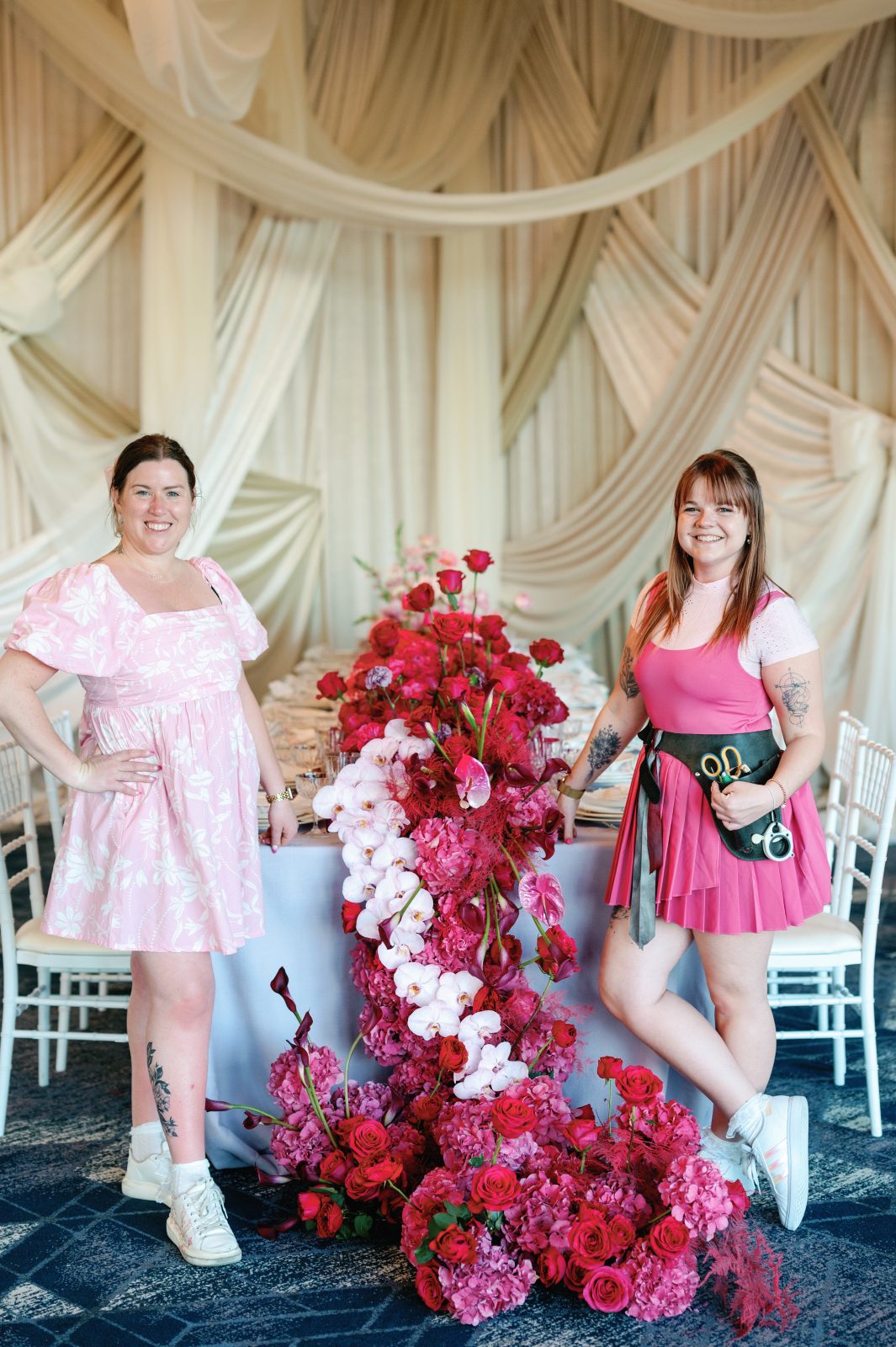 Travis and Erin standing either side of their ombre pink table scape with a stunning waterfall of pink blooms cascading down the front of the table.