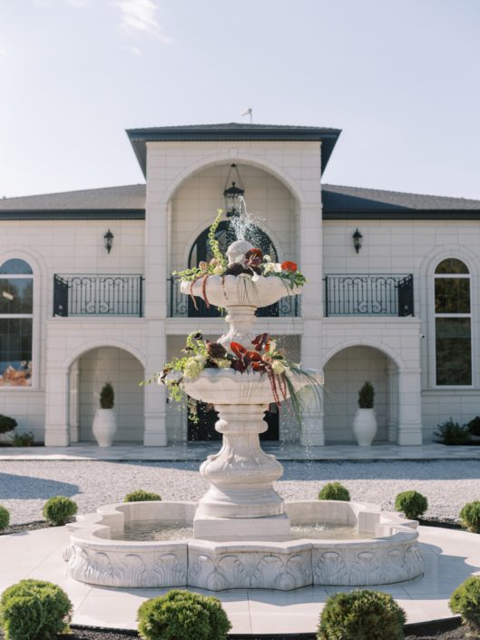 The stunning multilayered fountain in front of Archway Manor with lush floral arrangements in red, burgundy and green, displayed on the edges.
