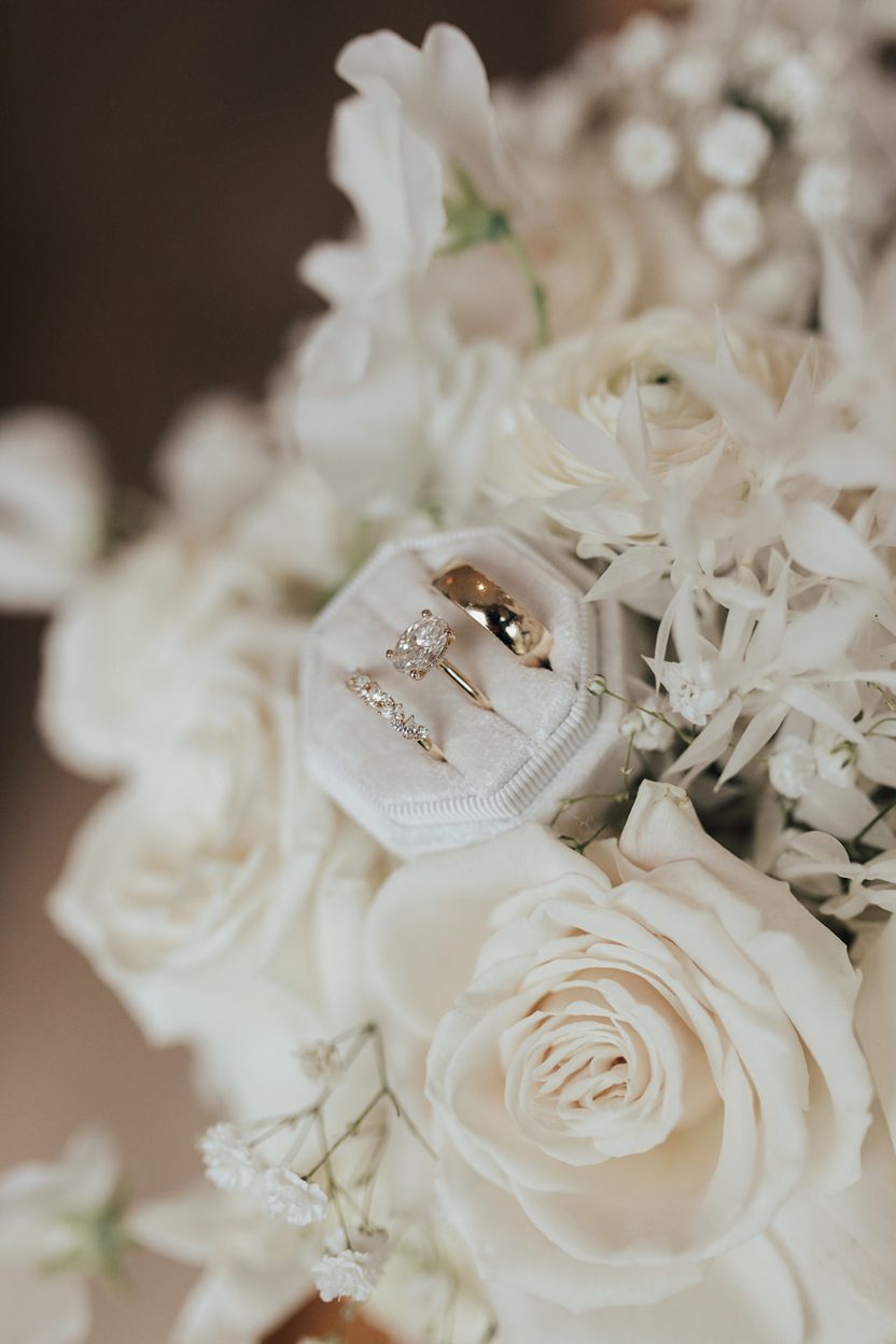 Rings A close up of a ring box containing the brides engagement ring and both the bride and groom's wedding bands tucked into a white floral arrangement.