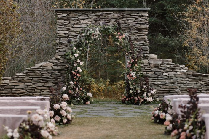 Ceremony set up of our "True to Hue" photoshoot, featuring a stunning rock arch adorned in flowers as well as big arrangements going down both sides of the aisle.